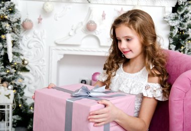 Çok güzel mutlu gülümseyen küçük kız çocuk prenses elbise Noel zamanında köknar ağacı yakınındaki hediye kutusu ile sandalyede oturan portresi