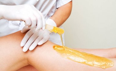 Cosmetologist beautician waxing female legs in the spa center be clipart