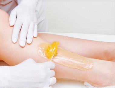 Cosmetologist beautician waxing female legs in the spa center be clipart