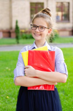 Okula dönelim. Eğitim konsepti. Okula giderken gülümseyen tatlı bir kız öğrenci. Kitapları tutan gözlüklü mutlu küçük kız. 