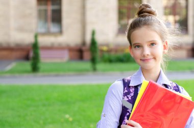 Okula dönelim. Eğitim konsepti. Okula giderken gülümseyen tatlı bir kız öğrenci. Sırt çantasıyla kitapları tutan mutlu küçük kız çocuğu.