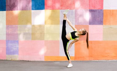 Spor kıyafetleriyle spor yapan genç bir kız duvarda yoga egzersizi yapıyor. Açık havada spor jimnastikçisi çocuk eğitimi. Sağlıklı yaşam tarzı ve vücut bakımı kavramı