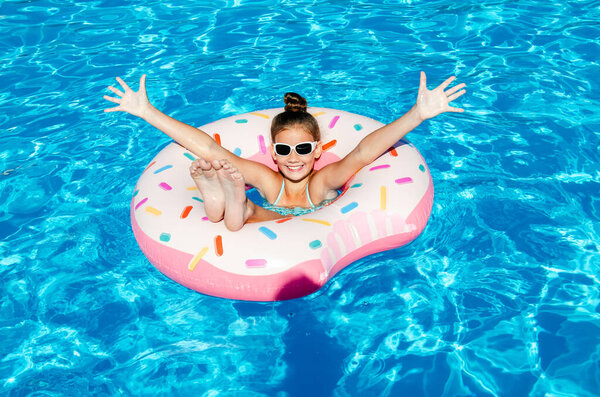 Cute smiling little girl in swimming pool with rubber ring. Child having fun on vacation in summertime