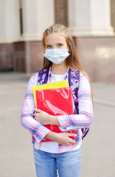 フェイスマスクとバックパックを持つ小さな女の子の子供 教育の概念 Covid 19の後に学校に戻る 屋外で本を保持する前の学生 — ストック写真