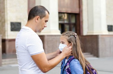  Eğitim konsepti. Covid-19 'dan sonra okula döndüm. Babası okula gitmeden önce kızına maske takıyor.