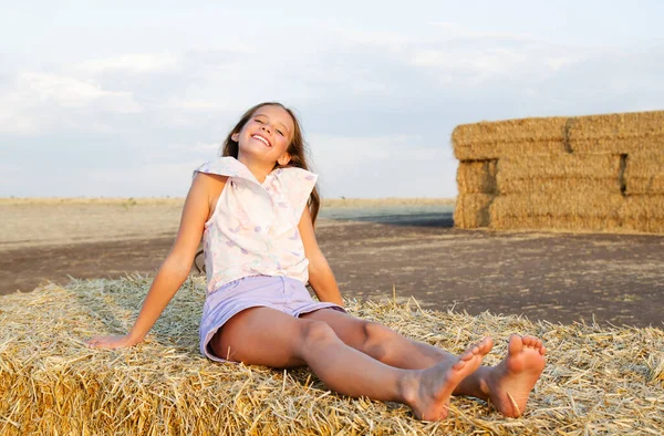 日落时分 坐在麦田里的干草堆上的可爱的笑容可亲的小女孩 — 图库照片