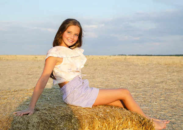 Suloinen Onnellinen Hymyilevä Pikkutyttö Istuu Heinän Päällä Vehnäpellolla Auringonlaskun Aikaan — kuvapankkivalokuva