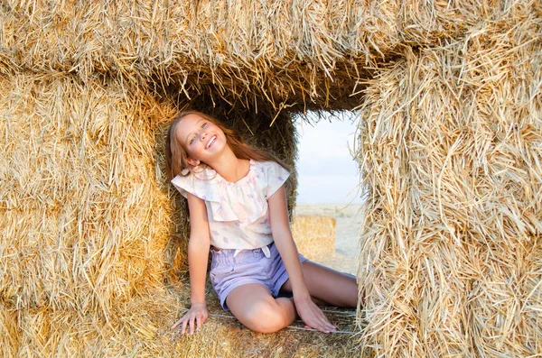 幸せな笑顔の女の子子供座っている干し草のロールに小麦畑で日没時 — ストック写真