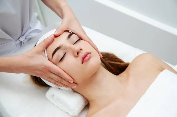 Beautician massaging woman\'s face. Attractive girl having facial treatment and massage. The young woman is lying and relaxingin. Beautiful female face receiving skin theraph