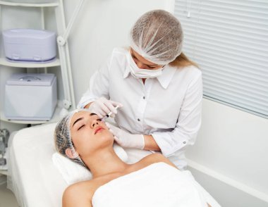 Kadın kozmetik yapıyor. Enjeksiyon. Güzellik iğneleri ve kozmetoloji. Güzellik salonunda genç bir kadın. Estetik cerrahi ve güzellik tedavisi.