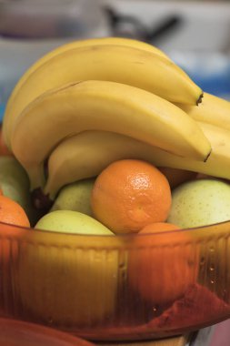 Muz, mandalina ve mutfakta bir kırmızı plastik vazo içinde yeşil elma