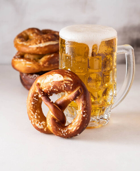 Свежеиспеченный домашний мягкий крендель с солью на белом столе со стаканом пива
.