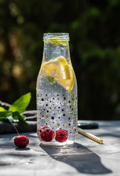 Fresh cherry cocktail. Fresh summer cocktail with cherry and ice cubes. Glass of cherry soda drink on dark stone background.