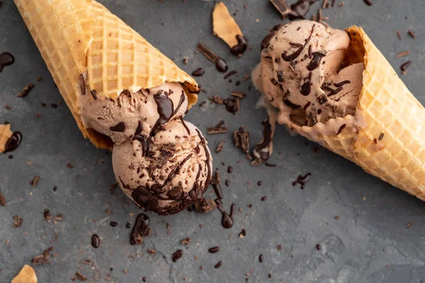 Homemade chocolate ice cream in waffle cones, with a spoon for ice cream, cocoa and pieces of dark chocolate. On a dark gray table. Copy space close view