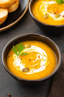 Taze kabak ile bir kase, sarımsak ve maydanoz otlar siyah bir zemin üzerine balkabağı çorbası. Sonbahar konsepti.