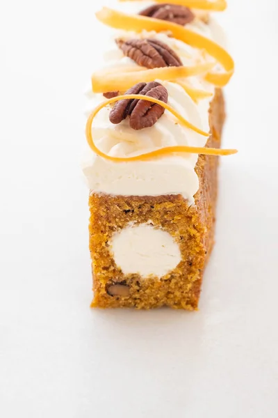 Carrot cake pie, sprinkled with nuts, decorated with cream-colored carrots on white marble.