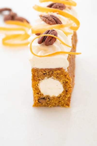 Carrot cake pie, sprinkled with nuts, decorated with cream-colored carrots on white marble.