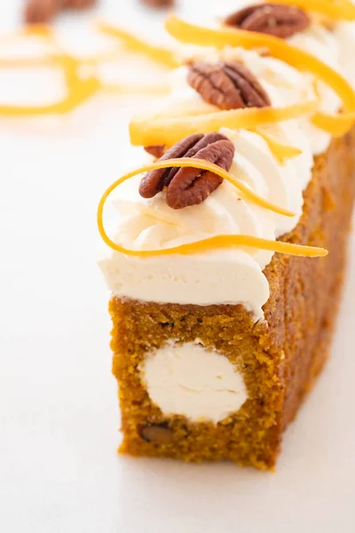 Carrot cake pie, sprinkled with nuts, decorated with cream-colored carrots on white marble.