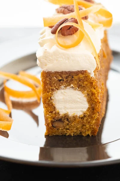 Carrot cake pie, sprinkled with nuts, decorated with cream-colored carrots on black marble.