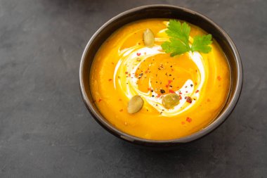 Taze kabak ile bir kase, sarımsak ve maydanoz otlar siyah bir zemin üzerine balkabağı çorbası. Sonbahar konsepti.