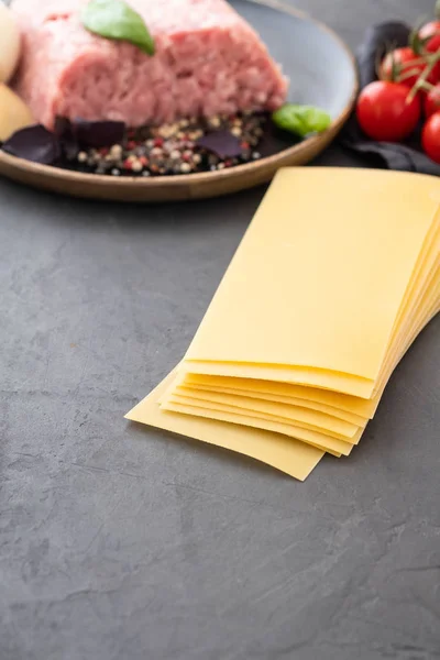 Ingredients for Italian lasagna with fresh cherry tomatoes and green basil leaves on sheets of dried pasta. Copy space. — Stock Photo, Image