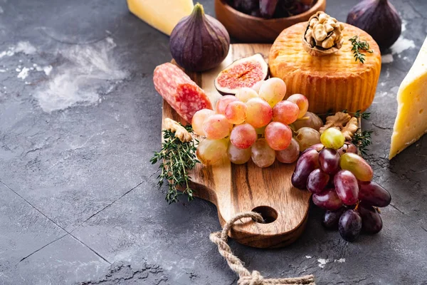 Cheese plate served with grapes, jam, figs, crackers and nuts on a grey background. Copy space. — Stock Photo, Image