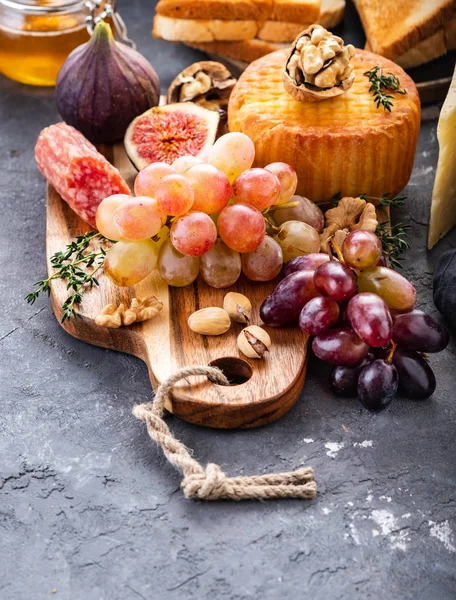 Prato de queijo servido com uvas, compota, figos, bolachas e nozes sobre fundo cinzento. Espaço de cópia . — Fotografia de Stock