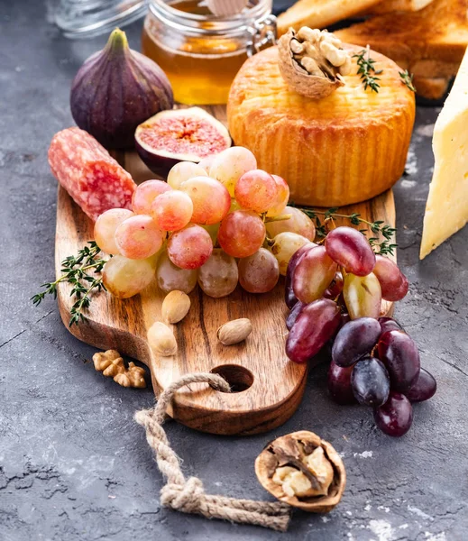 Prato de queijo servido com uvas, compota, figos, bolachas e nozes sobre fundo cinzento. Espaço de cópia . — Fotografia de Stock