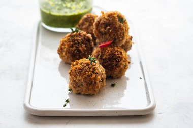 Beyaz arka plan üzerinde beyaz bir tabakta kekik ve yeşil soslu ev yapımı köfte.