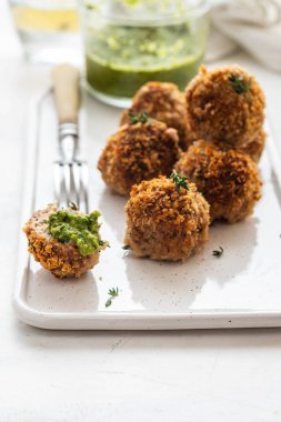 Beyaz arka plan üzerinde beyaz bir tabakta kekik ve yeşil soslu ev yapımı köfte.