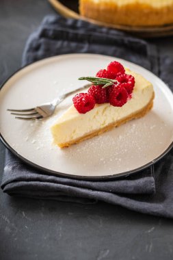 New York Cheesecake dilim ile ahududu karanlık bir arka plan üzerinde.