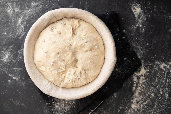 Baking bread. Dough in proofing basket on table with flour, sunflower seeds. Top view. — Stock Photo, Image