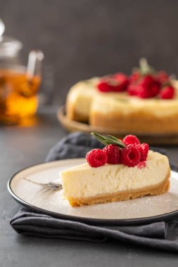 New York Cheesecake dilim ile ahududu karanlık bir arka plan üzerinde.