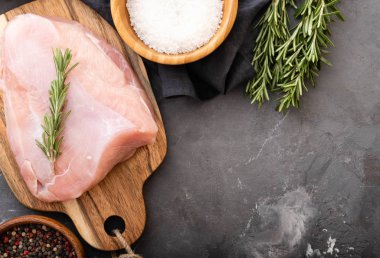 Baharat ve otlar ile siyah kesme tahtası üzerinde çiğ hindi fileto. Pişirme malzemeleri. Doğal sağlıklı gıda kavramı. Metin için yer ile üstten görünüm