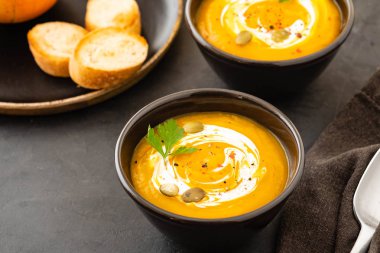 Taze kabak ile bir kase, sarımsak ve maydanoz otlar siyah bir zemin üzerine balkabağı çorbası. Sonbahar konsepti.