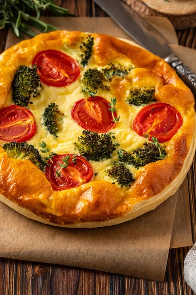 Vegetable pie with broccoli, peas, thyme. tomatoes and cheese on wooden background. Copy space.