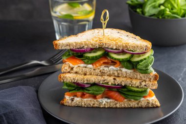 Krem peynir, somon ve ıspanak karanlık bir arka plan üzerinde sandviç.