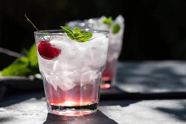 Cocktail di ciliegie fresche. Cocktail estivo fresco con cubetti di ciliegia e ghiaccio. Bicchiere di bibita alla ciliegia su sfondo pietra scura . — Foto Stock