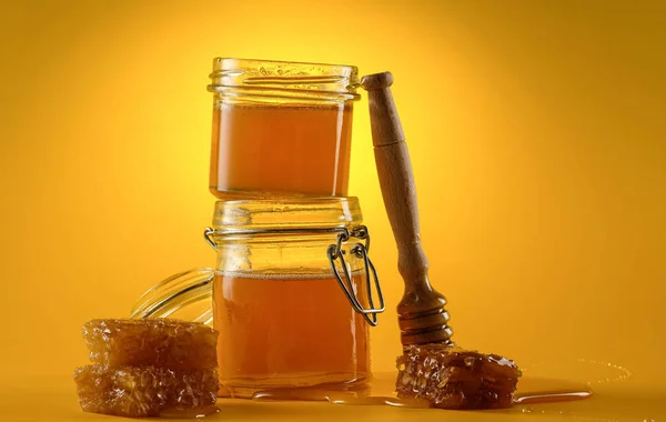 Two jars of honey with honeycombs and a stick on a yellow background. Copy space. — Stock Photo, Image