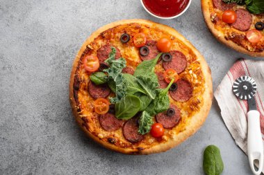 Lezzetli pepperoni pizza ve pişirme malzemeleri domates gri beton arka plan üzerinde fesleğen. Acı biberli pizzanın en iyi görünümü. Metin için kopyalama alanı ile.