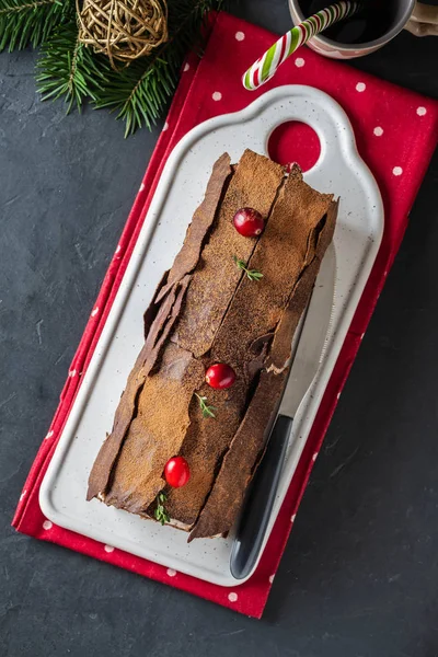Buche de Noel. Traditional Christmas dessert, Christmas yule log cake with chocolate cream, cranberry. On stone gray background with Christmas tree branches. — Stock Photo, Image