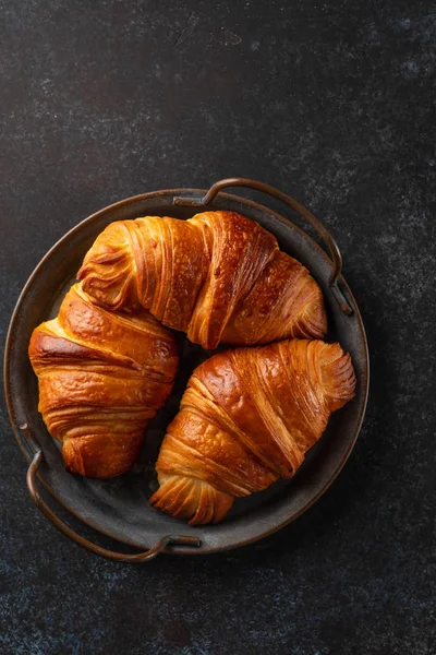 Croissants fraîchement cuits sur un plateau vintage. tas de croissants fraîchement cuits sur fond sombre. Pâtisserie française — Photo