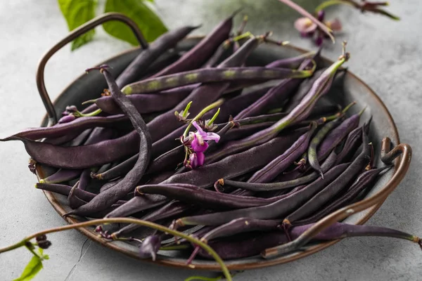 Purple string beans on metal tray, grey backround.