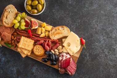 Pastırma, kurutulmuş et, sosis, zeytin, peynir ve üzümle ahşap bir tahtada servis tabağı. Üst görünüm.