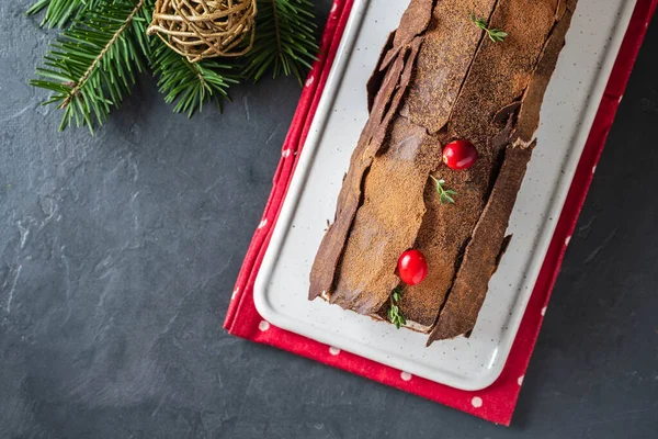 Buche de Noel. Postre tradicional de Navidad, tarta de Navidad con crema de chocolate, arándano. Sobre fondo gris piedra con ramas de árbol de Navidad. — Foto de Stock