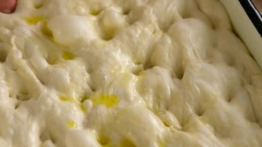Dişi eller hamuru pişirme tepsisine koyar, İtalyan ekmeğini hazırlar - zeytin yağı, domates, baharatlar, biberiye ve deniz tuzu ile Focaccia. Ekmek için Hamur. Focaccia - Pizza Focaccia hazırlanıyor. Yakın plan..