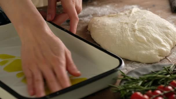 Las manos femeninas untan la bandeja para hornear con el aceite, preparan el pan italiano - focaccia con el aceite de oliva, los tomates, los condimentos, el romero y la sal marina. Masa para pan. Preparación de focaccia - Pizza focaccia . — Vídeos de Stock