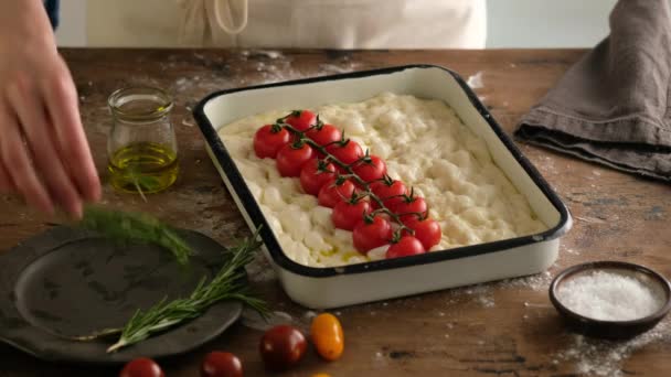 Le mani femminili posano un ramo di pomodoro ciliegia in pasta, preparano il pane italiano - la focaccia con olio d'oliva, pomodori, condimenti, rosmarino e sale marino. Pasta per il pane. Preparare la focaccia - Pizza . — Video Stock