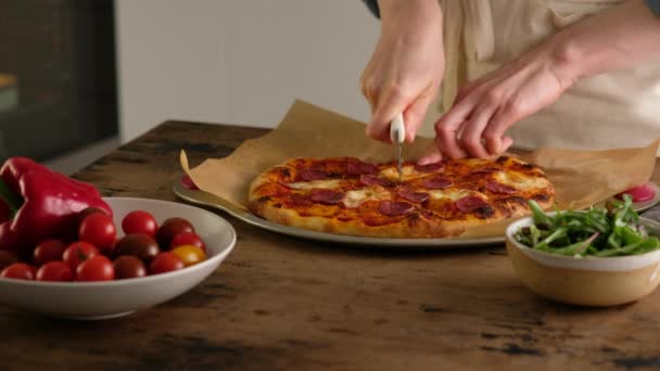 Le mani femminili tagliano la pizza a fette, preparano la pizza italiana con salsa, pomodori, condimenti, salsiccia piccante, spinaci, verdure, mozzarella di formaggio. Pasta per il pane. Pizza salame piccante . — Video Stock