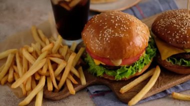 Fast food. Makro, hamburger, patates kızartması, kola. Bir kadın çörek, pirzola, marul, salatalık, domates, soğan ve sostan hamburger yaptı. Güzel arka plan. Yavaş çekim.